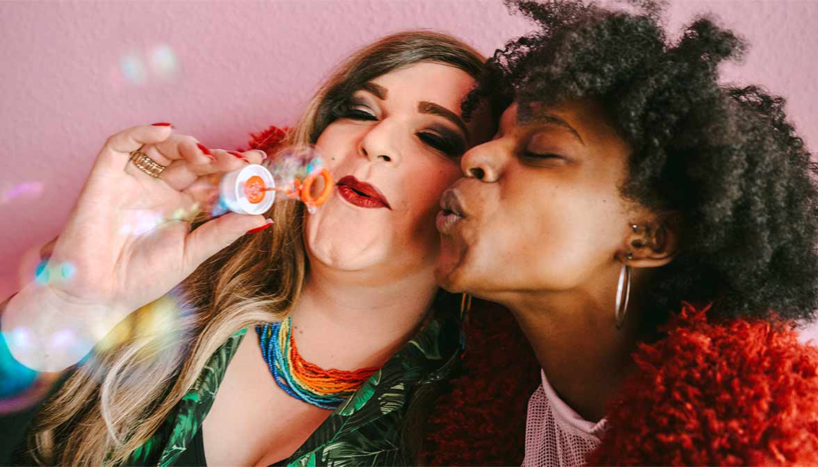 Two women blowing bubbles in front of a pink wall