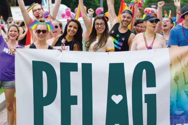 People holding up a PFLAG flag at a Pride event